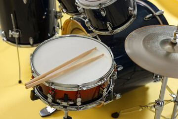Modern drum kit with drumsticks on yellow background, closeup