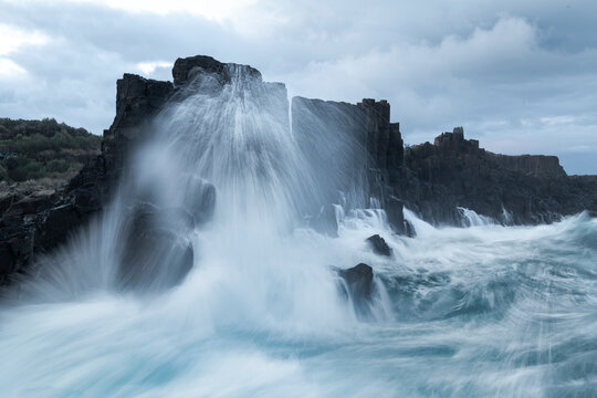Powerful ocean waves crashing over dark basalt rocks at Bombo Quarry, Kiama, New South Wales, Australia. Dramatic coastal seascape with motion blur water.