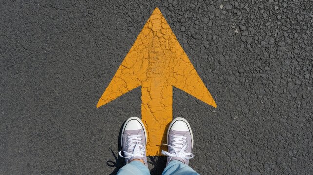 Person in sneakers stands on a bright yellow arrow on asphalt pointing forward under sunlight