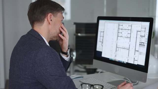 Businessman stressing at his office desk, covering face with hands. Feeling tired, having a headache from work overload. Business and architecture concept