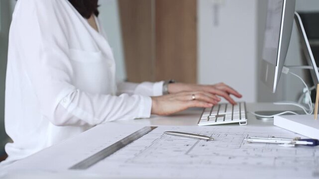 Architect creating new designs, working at a computer in office with blueprints and drafting tools. Business and architecture concept