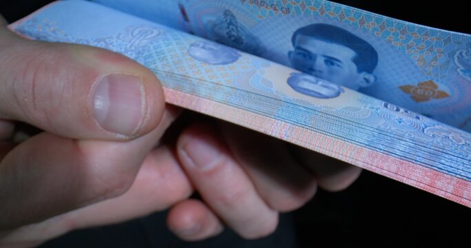 Holding a banknote in hand showing currency design and portrait of leader in dim lighting