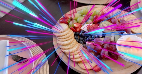 Showing wooden platter with crackers, grapes, strawberries, cheese, dip on dark table, neon streaks