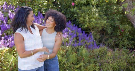 Smiling mother and daughter hugging in garden near purple shrubs, wearing jeans and wrist bangles