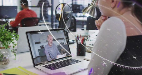 Woman in black top watching laptop in open office, presenter holding papers on screen, copy space