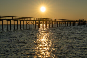 Fototapeta premium Sunset over the pier with reflections on water during evening hours in a coastal area