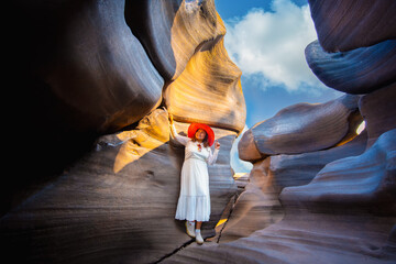 Woman in white dress and red hat explores canyon with smooth rock formations and potholes under bright blue sky Lei Dan Stone Field Thailand