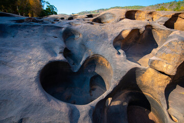 = Natural rock formations with deep potholes carved by erosion sunlight scenic outdoor landscape with trees and hills Lei Dan Stone Field Thailand