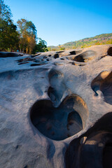Heart shaped potholes carved in smooth rock surface under clear blue sky with trees and hills in background Lei Dan Stone Field Thailand