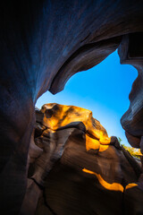 Sunlight illuminates smooth canyon walls with shadows creating warm contrast against blue sky and potholes in rock Lei Dan Stone Field Thailand