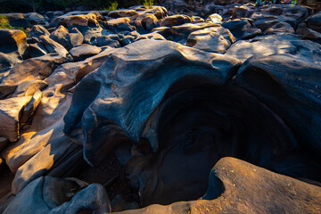 Natural rock formation with potholes carved by water erosion under warm sunlight creating textured surface Lei Dan Stone Field Thailand
