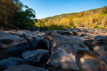 Rock formation potholes in riverbed with forest and hills under clear blue sky Lei Dan Stone Field Thailand