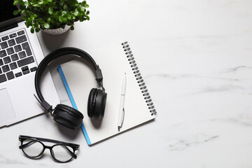 Headphones, laptop, glasses, stationery and floral decor on white marble table, flat lay. Space for...