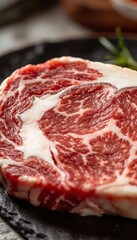 Close-up of a marbled raw ribeye steak with visible fat marbling on a dark plate