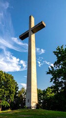 Large concrete cross monument against blue sky with trees in the foreground