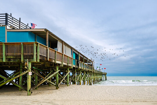 Sea birds fly above the wooden Pier 14 along the Grand Strand sandy beach of the Atlantic Ocean at Myrtle Beach, South Carolina.