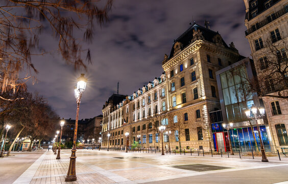 Place Louis Lepine square features historic lamp posts and the illuminated facade of the Prefecture of Police building on Ile de la Cite in Paris, France