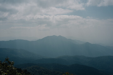 Obraz premium A muted, atmospheric view of distant, hazy mountains under a cloudy sky. Layers of blue and gray create a sense of depth and solitude.