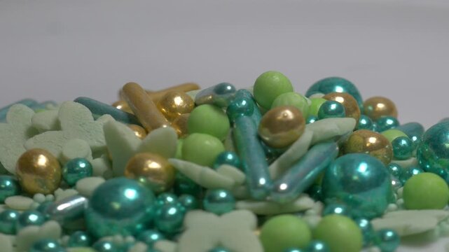 A heap of cylindrical sweet sprinkles in white and gold colors rotates on a plain surface, showcasing their texture and shimmering finish for cake decoration.