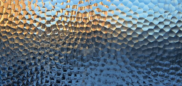 Abstract textured glass surface with blue and golden light patterns. Geometric frosted glass distortion creates a modern aesthetic, perfect for creative backgrounds and design