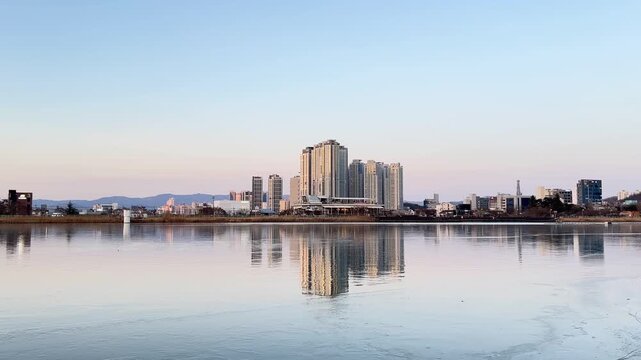 Daegu, South Korea &ndash; February 8, 2026: City buildings of Daegu are reflected on the frozen surface of Suseong Lake during winter. Pedestrians walk along the shorelin
