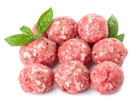 Freshly formed uncooked meatballs with vibrant basil leaves on a bright white background
