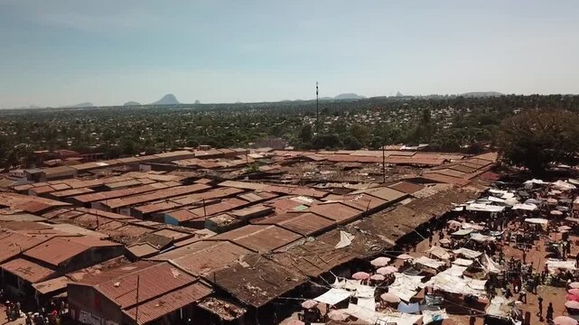 Aerial cityscape of Nampula, Mozambique showing a dense open-air market with rows of tin-roofed stalls and crowds gathered along the market edge.​
