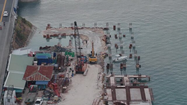 Busy causeway bridge construction over blue waters near Tagbilaran City, cranes move to dredge and fiell, aerial medium static