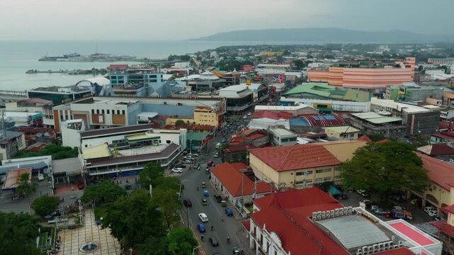 Steady traffic flows along CPG North national highway in Tagbilaran City, aerial medium tracking pan left, vibrant colorful homes