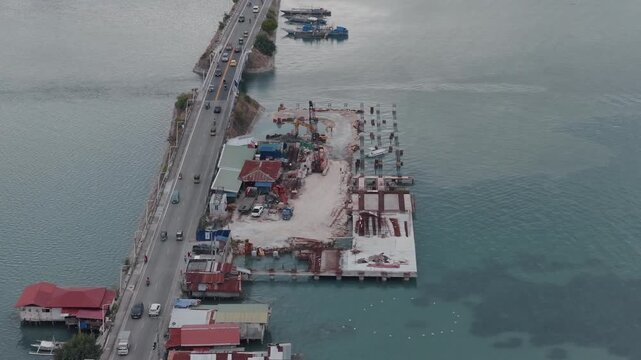 Long bridge stretches across coastal water linking Tagbilaran and Dauis with construction site dreding operation on edge, aerial orbit