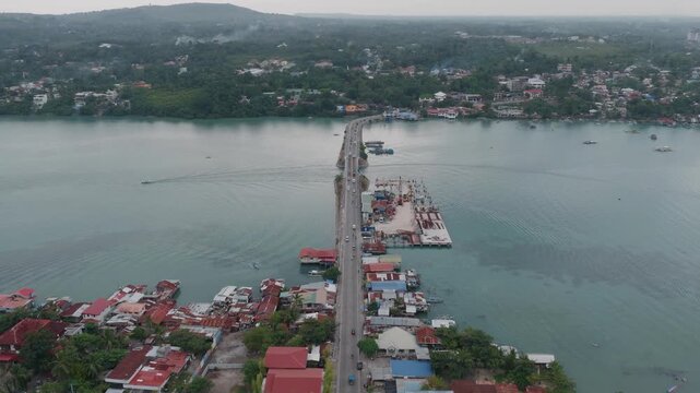 Bridge roadway crosses calm coastal waters toward Dauis from Tagbilaran City, panoramic aerial dolyl establish