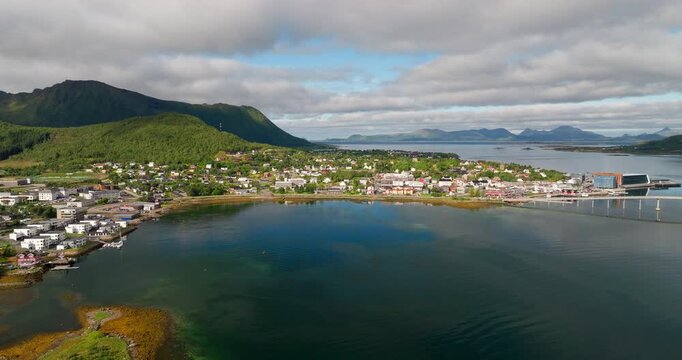 Establishing drone shot of coastal town of Stokmarknes in Vester&aring;len archipelago, harbor, bridge, and surrounding mountains, Norway. Aerial panoramic view
