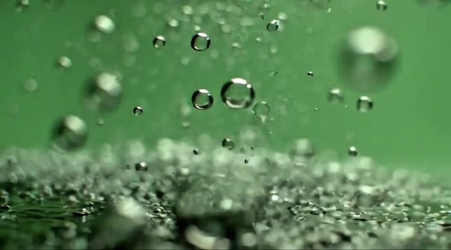 A dynamic macro shot of translucent liquid droplets and bubbles suspended mid-air against a soft emerald green backdrop.