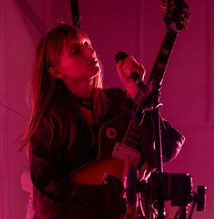young lady singing and playing guitar in rocker clothes with red backlight