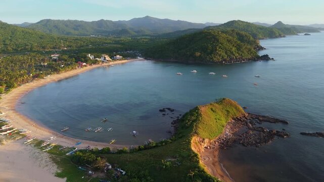 Cinematic aerial drone shot showing the unique twin beach formation and lush green hills of Nacpan Beach in El Nido, Palawan. Tropical paradise scenery in the Philippines