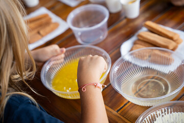Kids making tiramisu dessert at cooking workshop, hands preparing ingredients on wooden table, family culinary class and learning concept