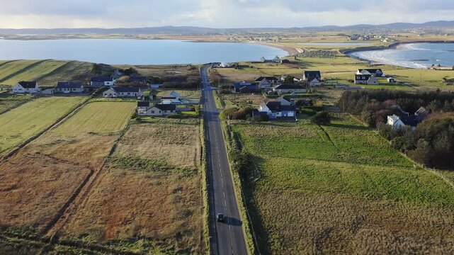 Drone shot tracking a car driving along the Braighe road towards Stornoway.