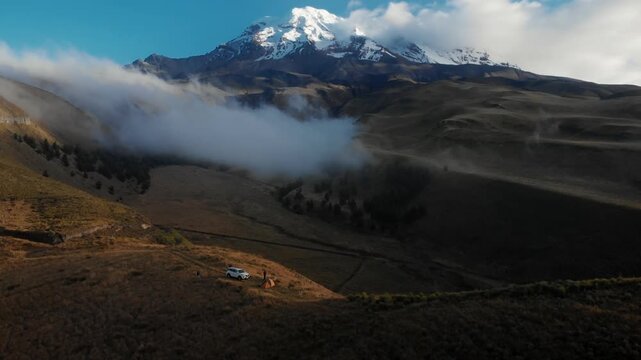 Chimborazo, Ecuador. A huge volcano with snow in the middle of a beautiful mountain range. Soft drone movement. Shiny day with some clouds.