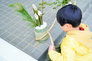 屋外で手作りした小さい門松の注連縄を結ぶ幼児、日本の伝統行事、お正月の準備