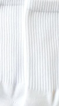 A pristine pair of new, white ribbed crew socks lies neatly arranged against a vibrant, solid yellow background, creating a visually striking contrast. The clean, soft cotton texture of the hosiery is