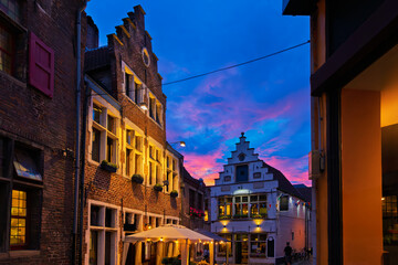 Fototapeta premium Illuminated traditional Belgian gabled houses and cafes on a charming, narrow, cobbled alley in the historic Patershol district of Ghent Belgium at twilight.