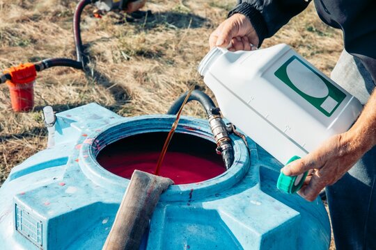 men's hands pouring chemical into a large blue plastic tank filled, agricultural mixing process, chemical transfer in sunny rural field, agriculture, irrigation, fungicides