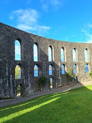 Fototapeta premium Stone arches of McCaig’s Tower in Oban, Scotland. The historic granite structure, inspired by Roman architecture, frames views of the sea and surrounding islands through its repeating arched openings.