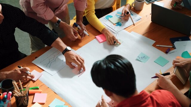 Top view of business team in casual cloth hand writing idea on sticky notes. Closeup of diverse people brainstorming marketing idea while sticking colorful sticky notes on mind mapping. Convocation.