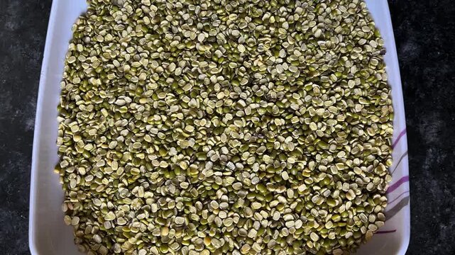 Top view of raw split green gram (Moong Dal) on a white square plate over a dark granite surface