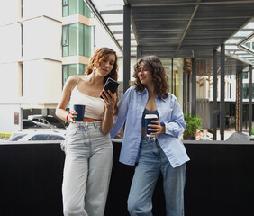 Two young women drink coffee and take pictures near the entrance to the office.