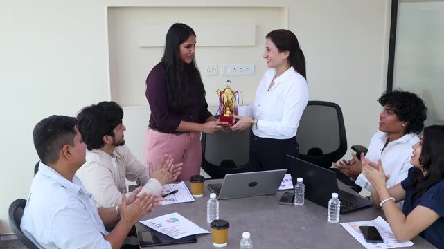 Young indian colleagues in office meeting room are applauding, celebrating, and acknowledging a dedicated businesswoman receiving an award for her achievement and success. Corporate job opportunity.4k