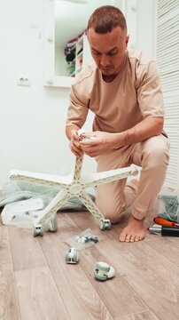 Person assembles armchair at home, holding wheels and tools while preparing parts for installation. DIY concept, flat pack furniture and home improvement.