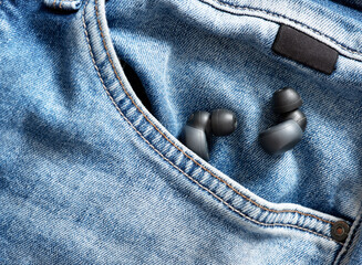 Wireless earbuds resting in blue jeans denim pocket