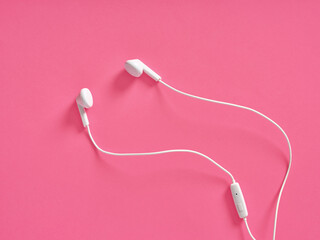 White wired earbuds resting on pink background